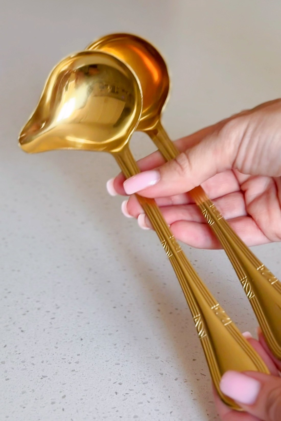 Two small gold sauce ladles held in one hand over a pale counter.