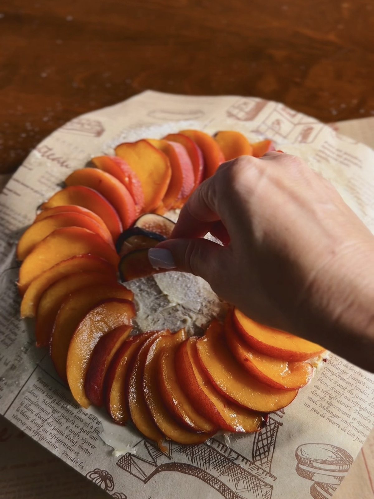Arranging sliced peaches and fresh figs in a circle on buttered parchment paper