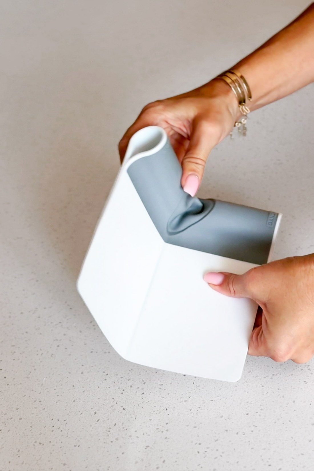 White and grey folding bench scraper being flexed open by two hands on a pale counter.