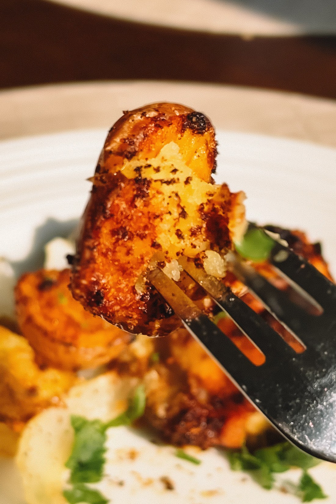 A crispy golden air fryer baby potato on a fork above a plate of chicken and potatoes
