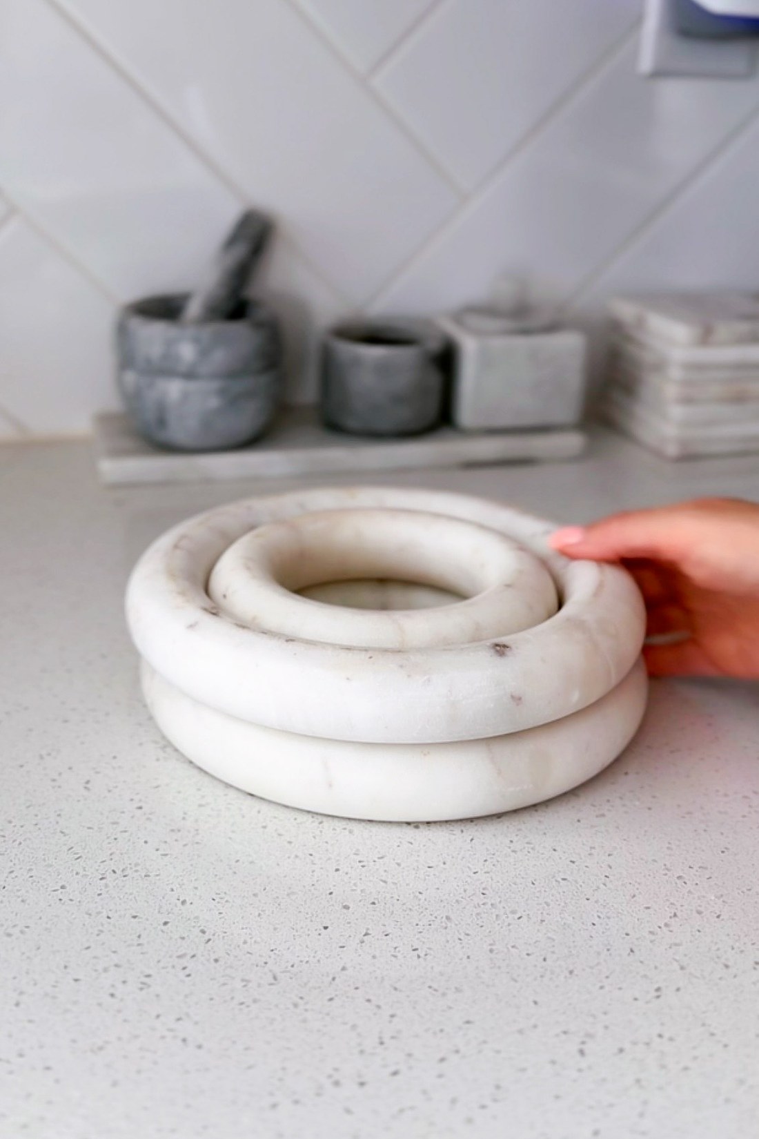Two round white marble trivets stacked on a pale speckled counter in front of a white tile backsplash.