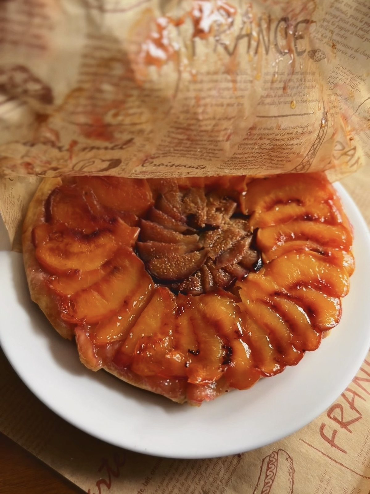 Peeling the parchment back off the flipped tart to reveal caramelized figs and peaches