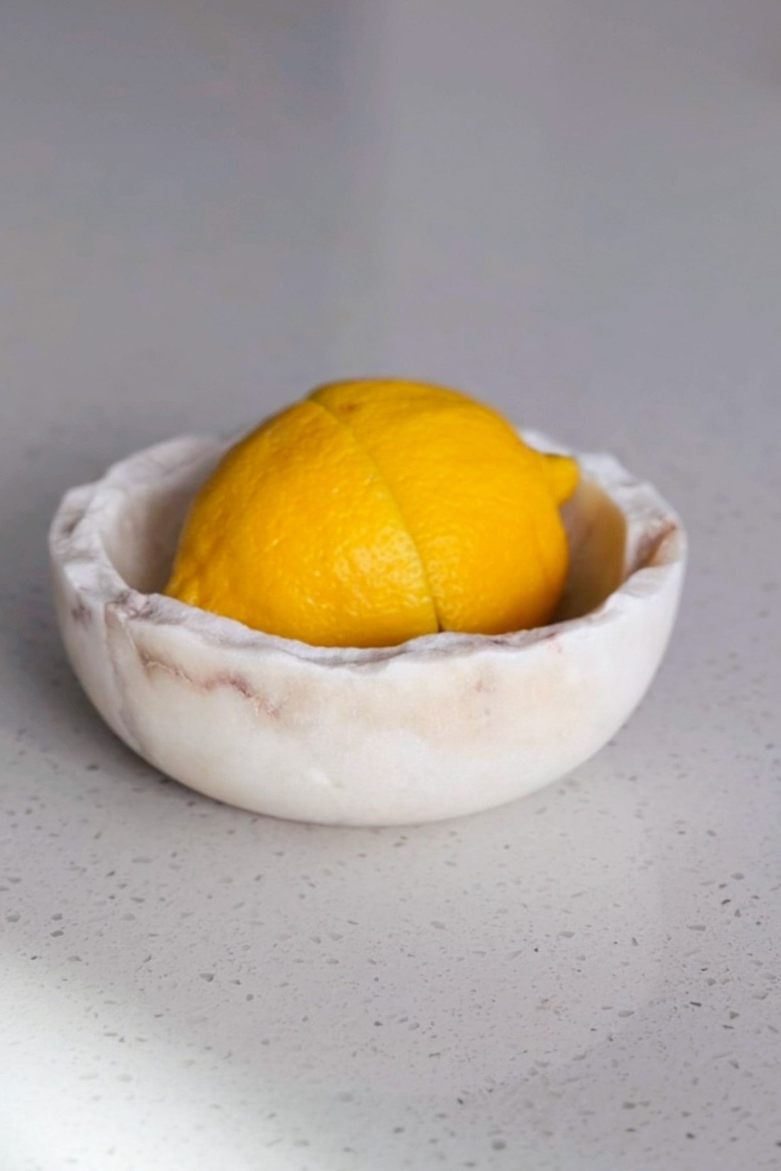 Small white marble bowl holding a single lemon on a pale counter.