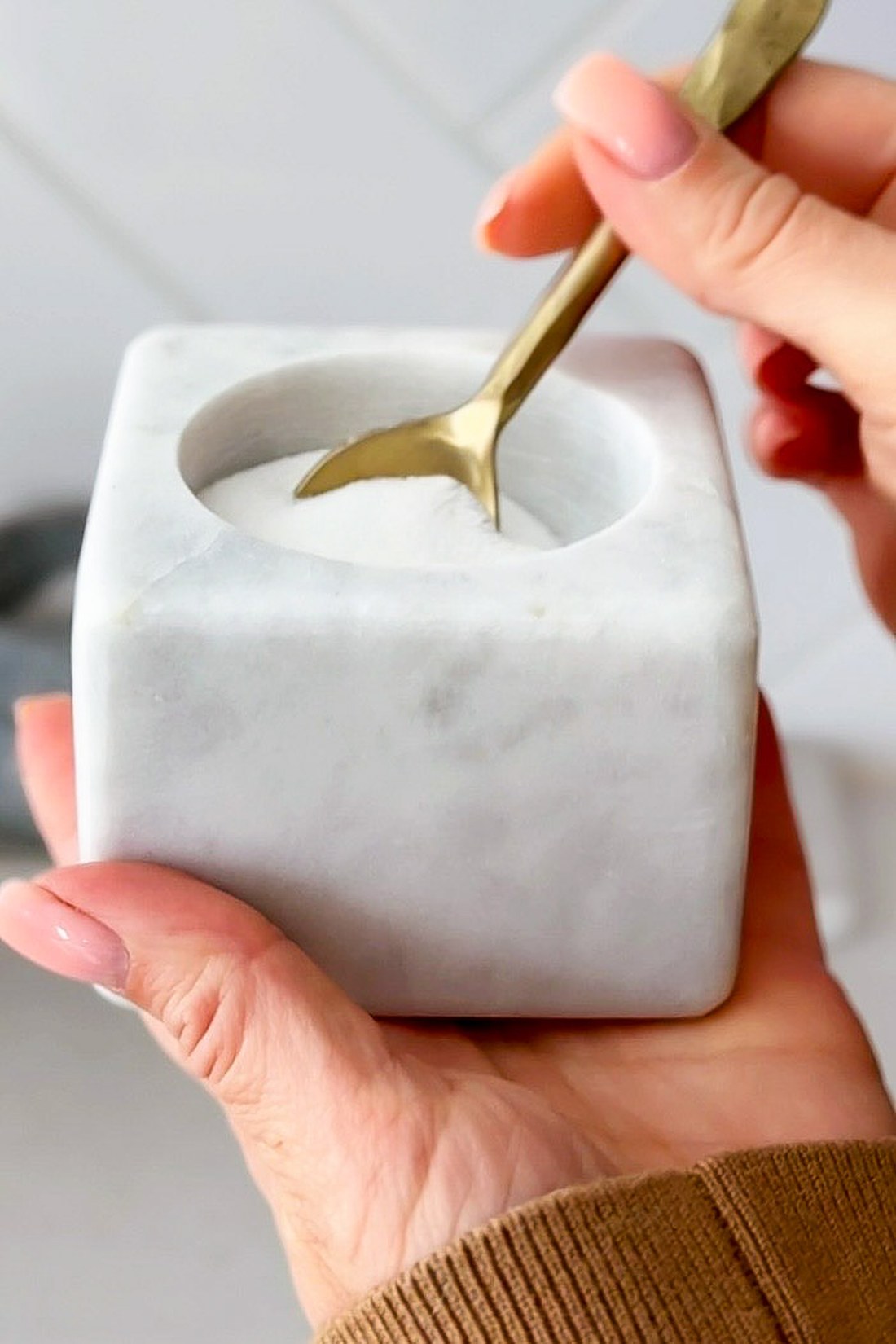 Square white marble salt cellar filled with salt, with a small brass spoon resting in it.