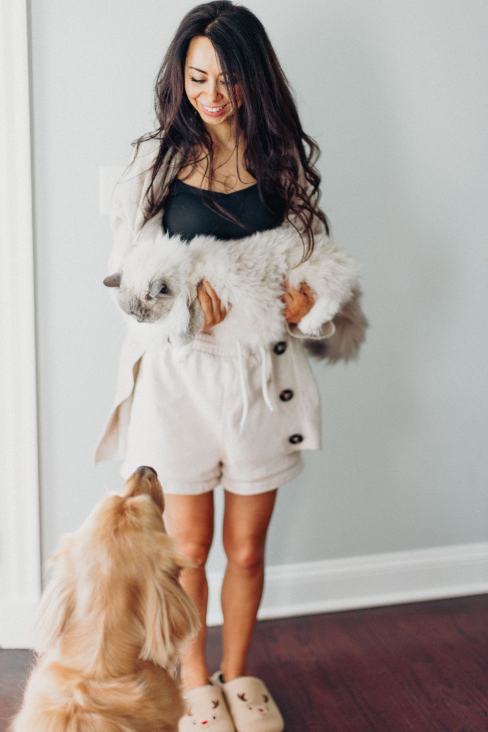 Olya standing in a hallway holding a fluffy grey and white cat, with her golden retriever looking up at her from the floor.