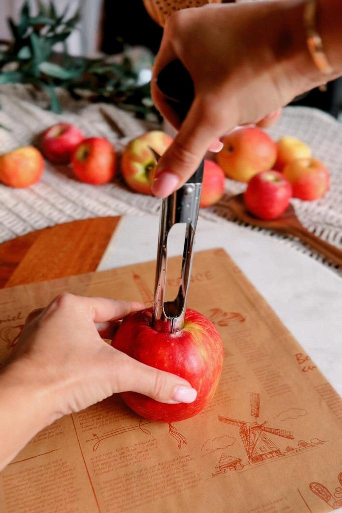 Stainless steel apple corer being pressed into a red apple on a wooden board