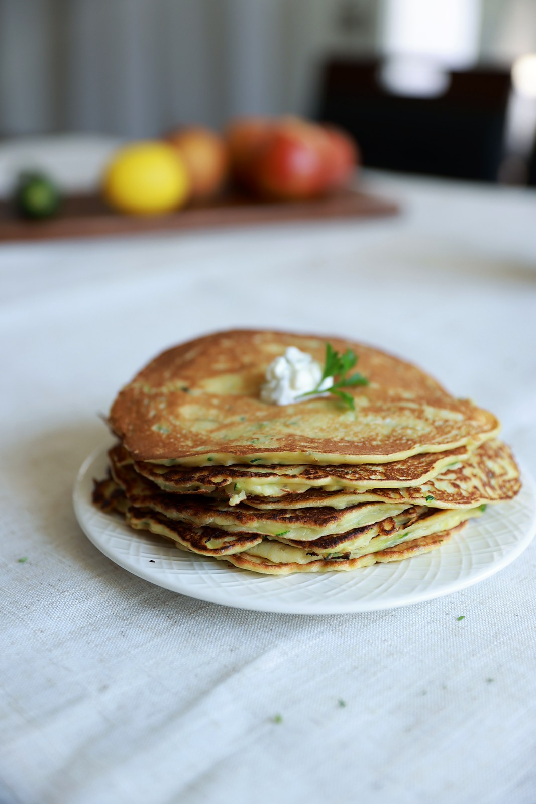 A stack of golden zucchini pancakes on a white plate topped with garlic yogurt and parsley.