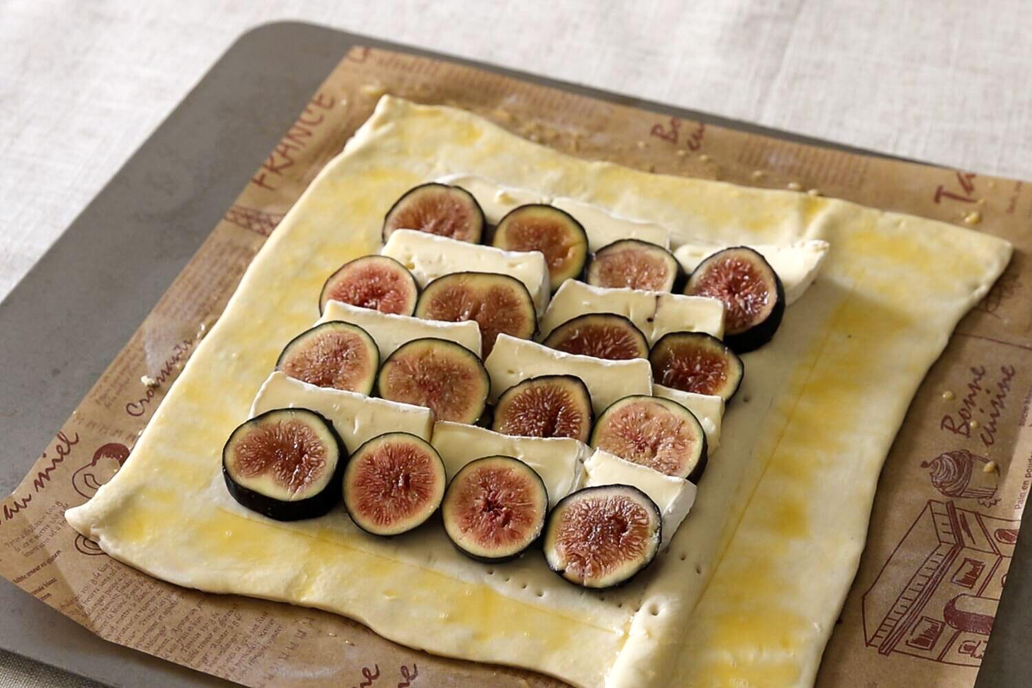 Rows of sliced brie and fresh figs laid out on raw puff pastry with an egg washed border, ready for the oven.