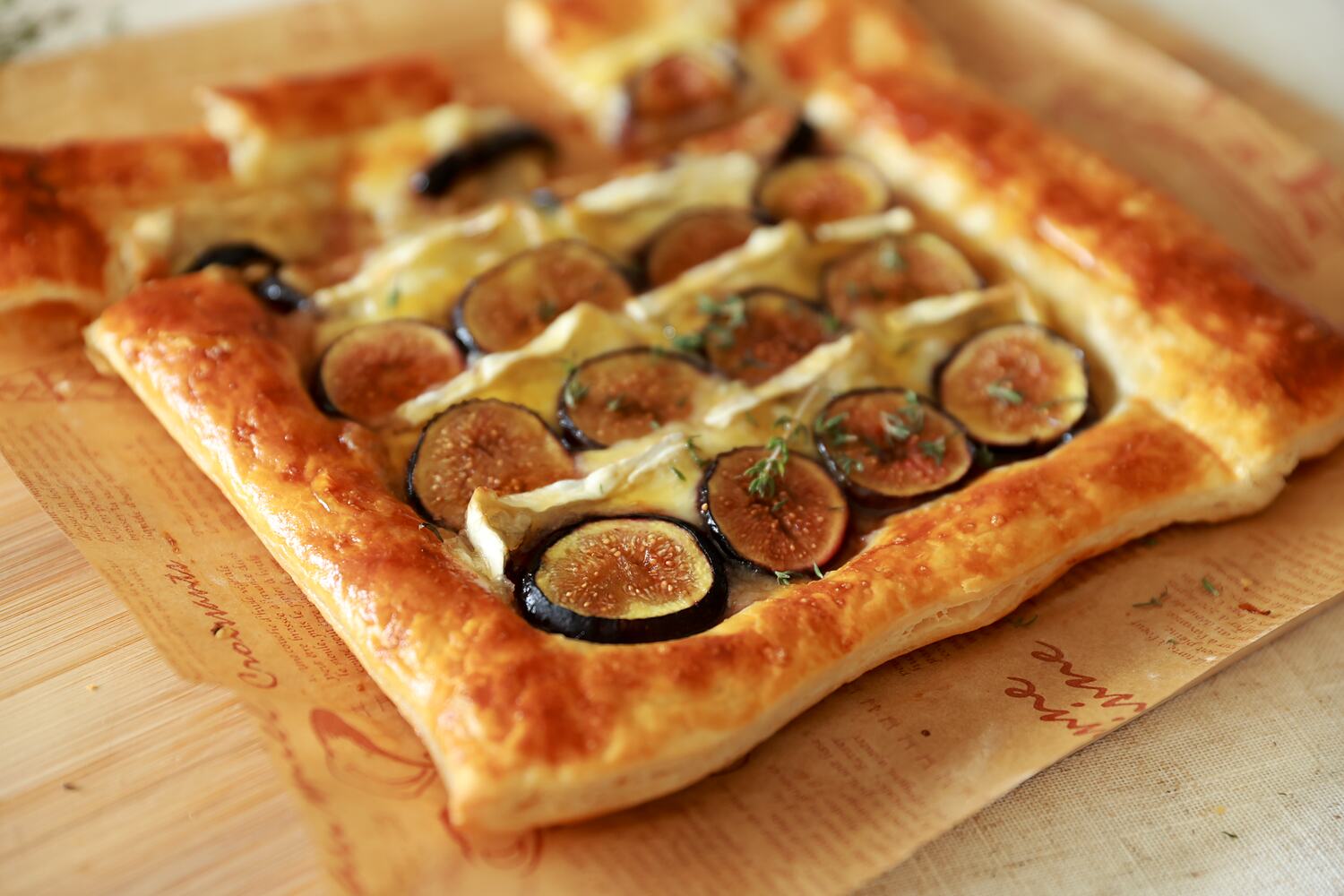 Close up of a golden fig and brie puff pastry tart topped with fresh thyme.