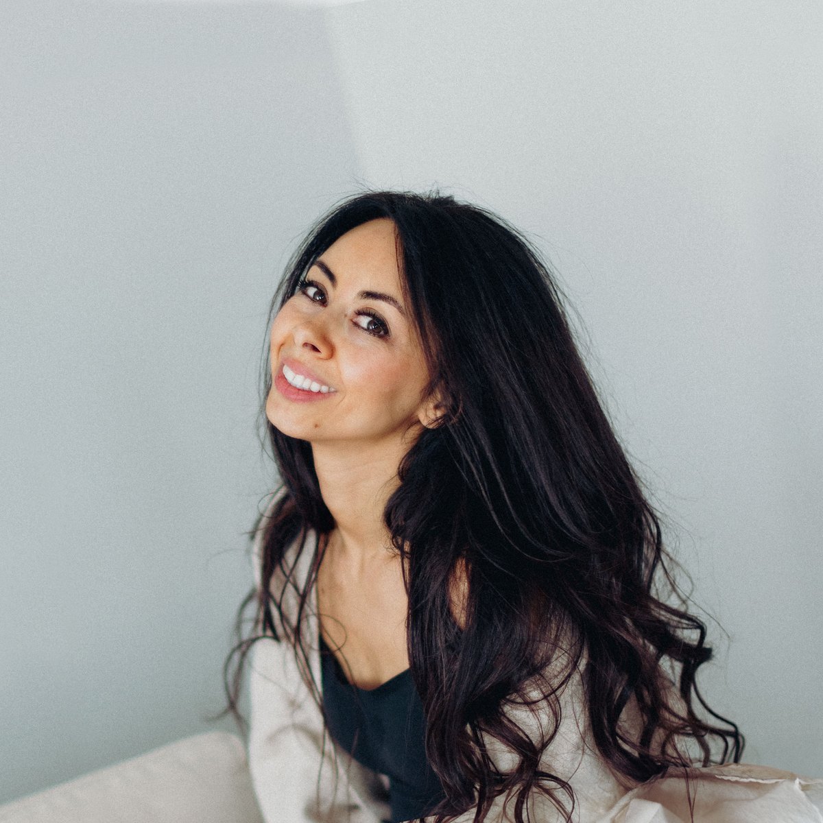 Olya, smiling and looking up, against a pale grey wall.