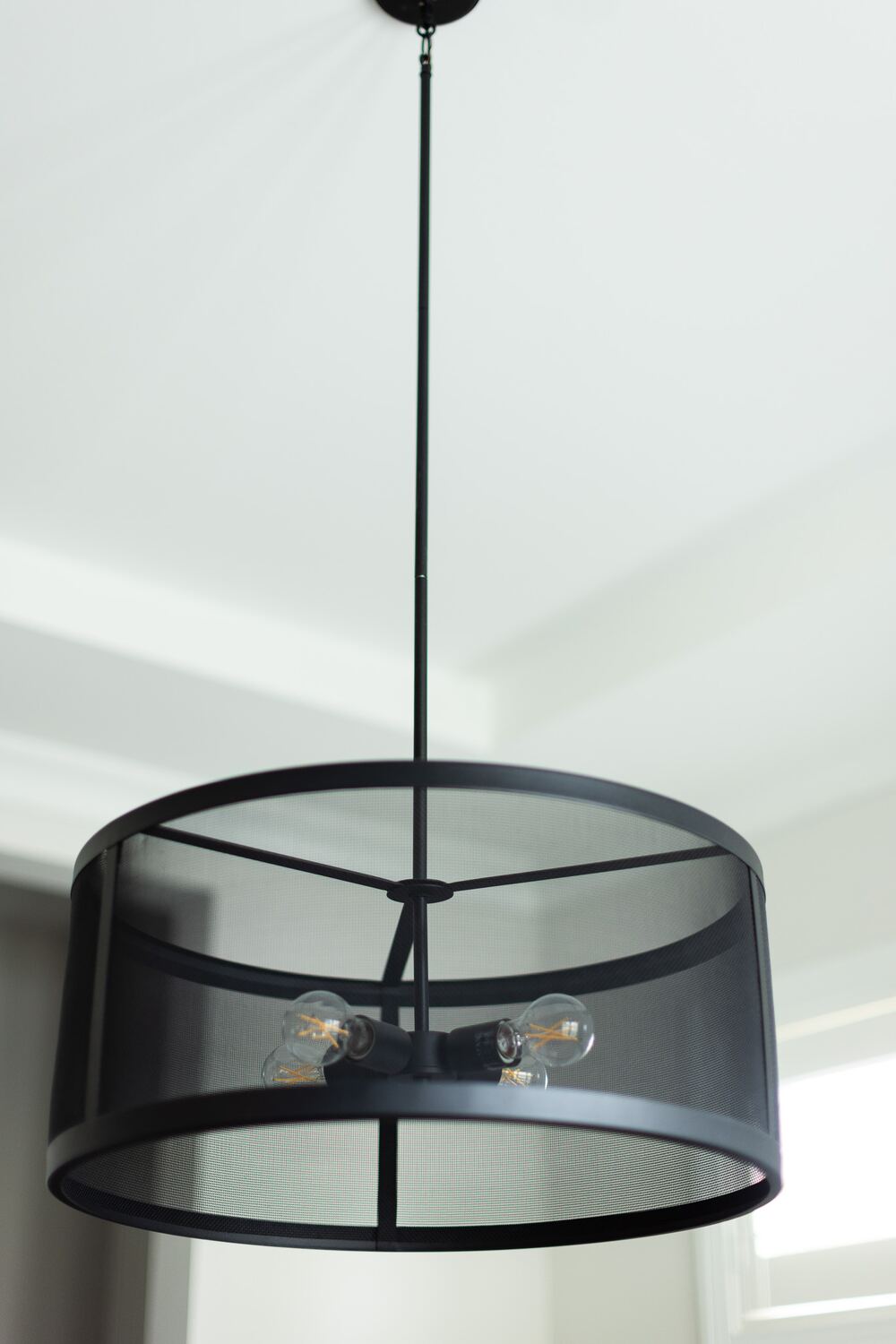 A black mesh drum pendant light with exposed filament bulbs hanging from a white ceiling.