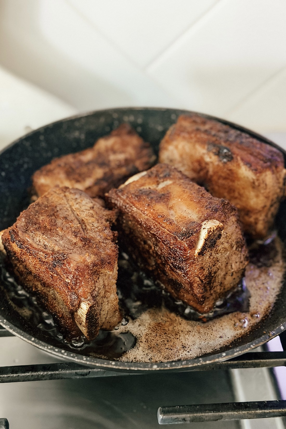 Beef short ribs browning in a hot skillet until deeply golden on all sides