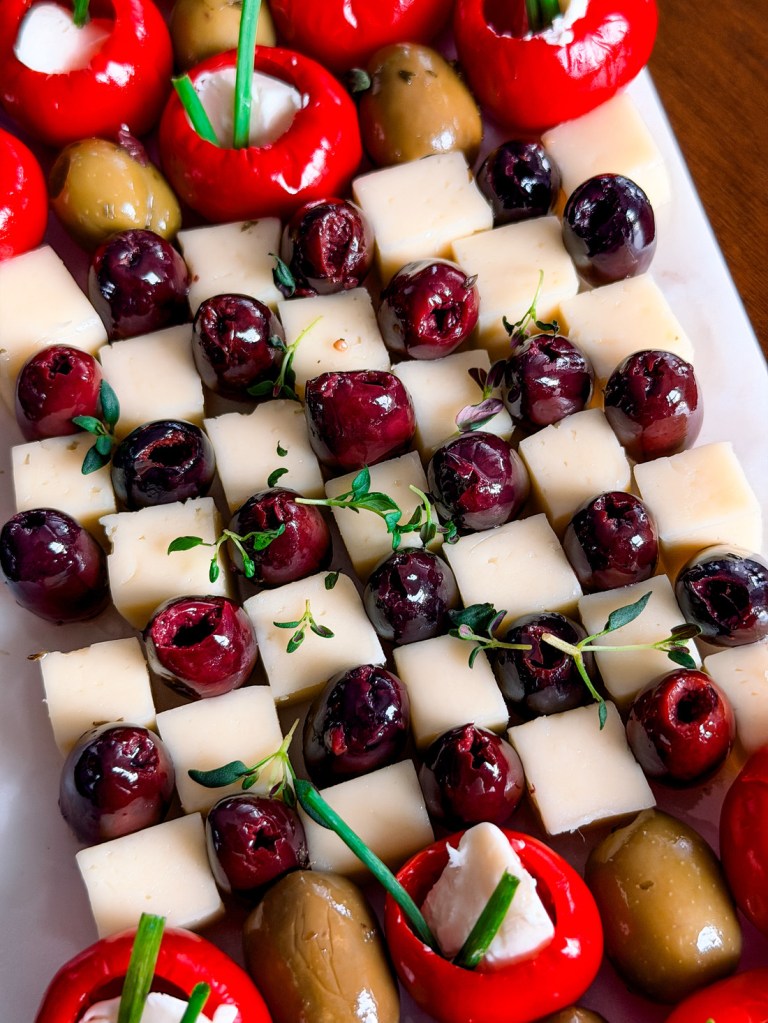 Close up of a checkerboard appetizer board with dark olives and white cheese cubes in alternating rows