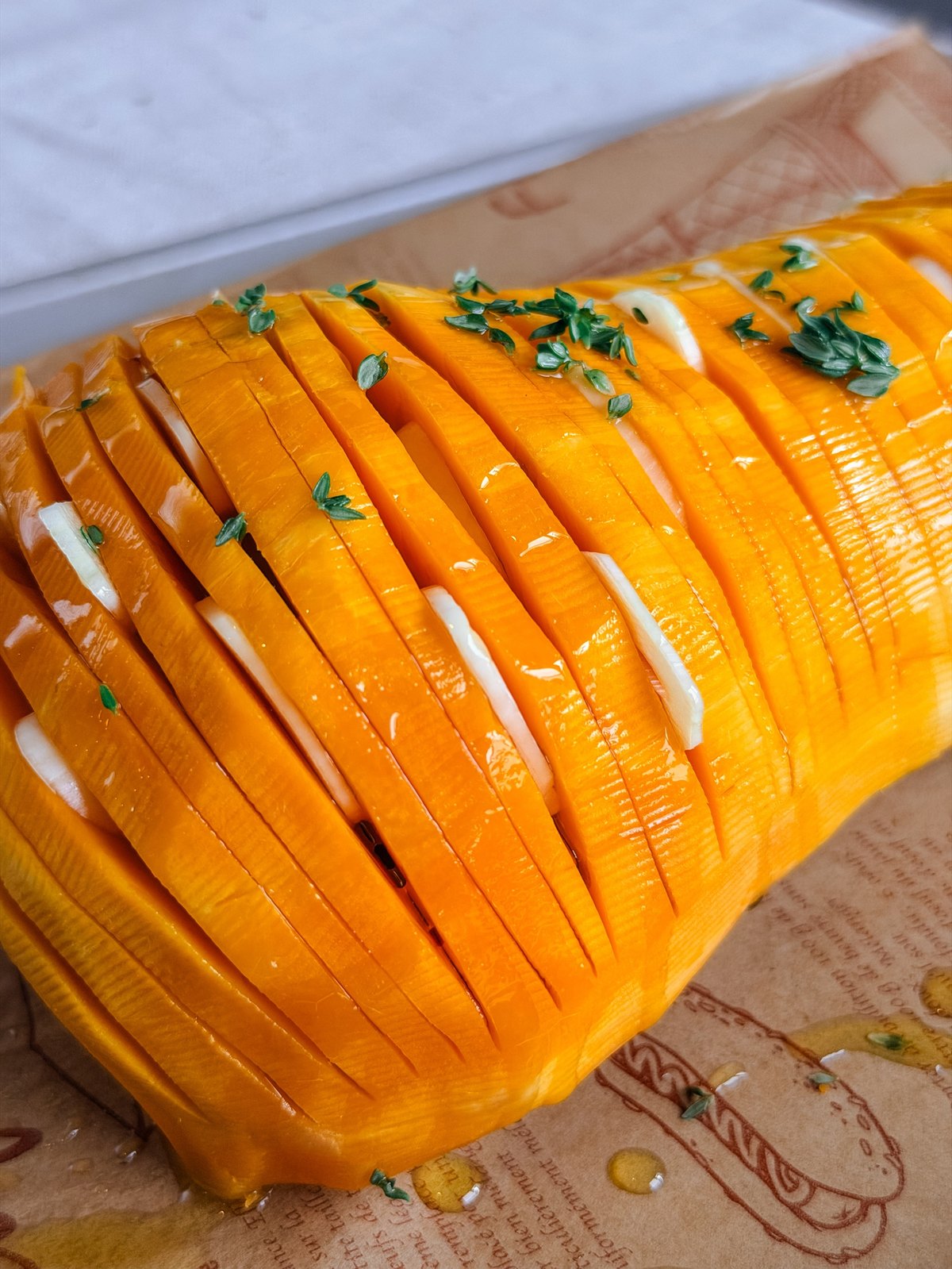 Close up of raw butternut squash sliced hasselback style with melted butter sitting in each cut