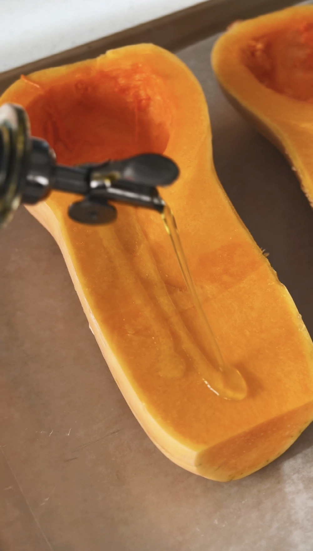 Olive oil poured over the cut side of a halved butternut squash on a sheet pan