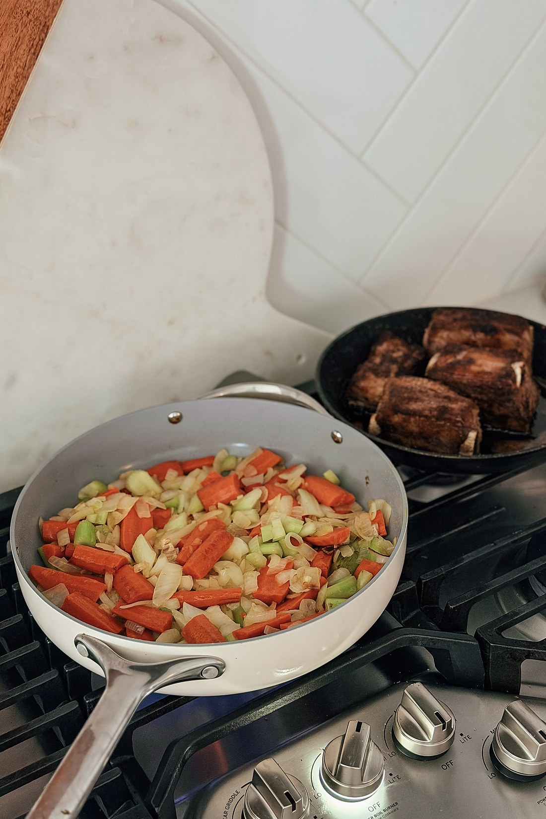 Onion, carrots and celery softening in a pan next to the browned short ribs