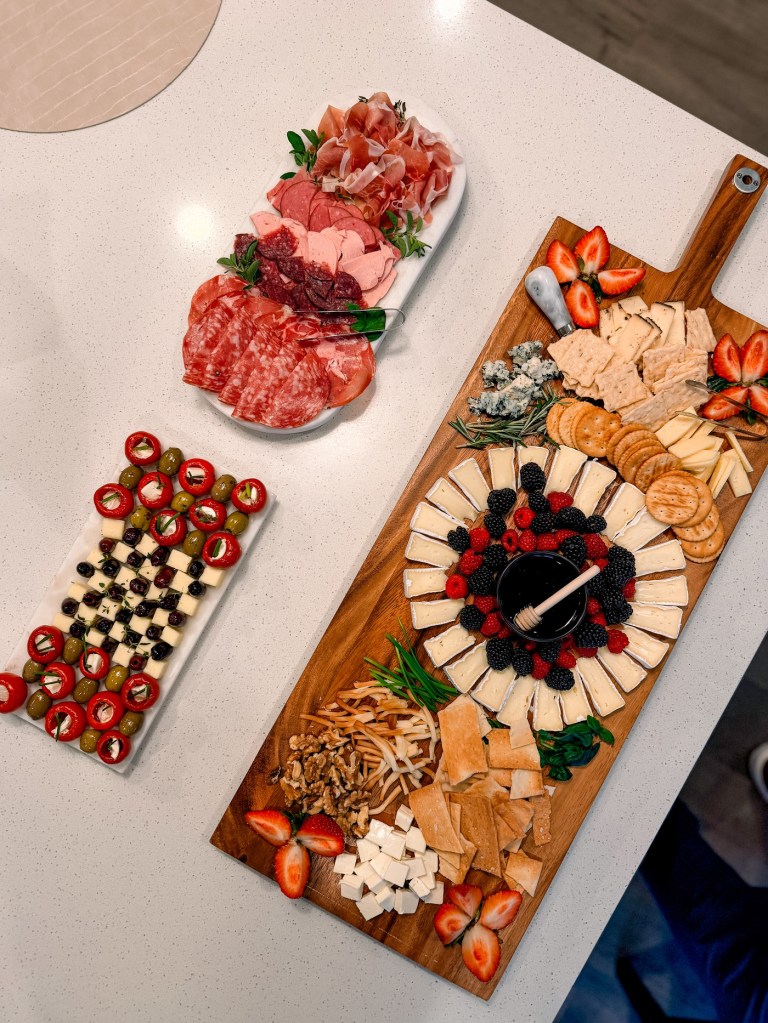 A full no cook appetizer spread with a checkerboard olive and cheese platter, a meat platter and a wooden board with brie, crackers and berries