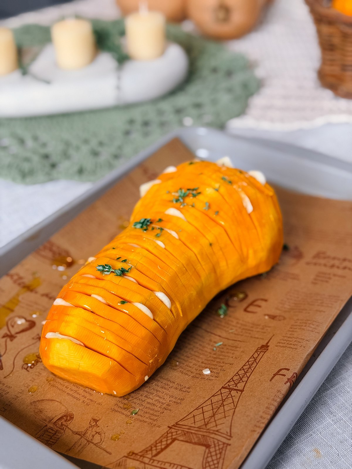 Raw hasselback butternut squash on a sheet pan with candles, small pumpkins and a basket on an autumn table