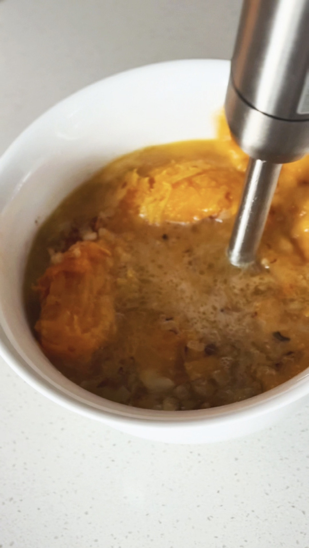 Blending the roasted squash and broth with an immersion blender in a white bowl