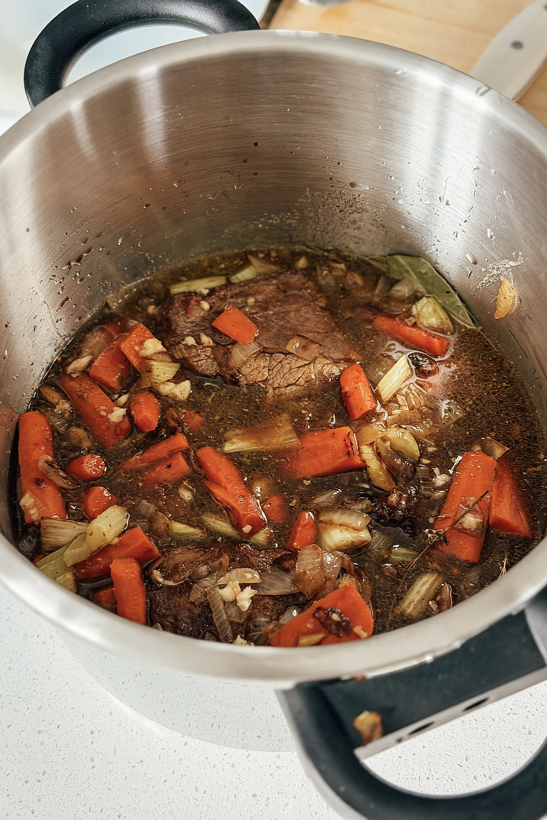 Short ribs, carrots, celery and bay leaves in the pressure cooker with red wine and beef broth