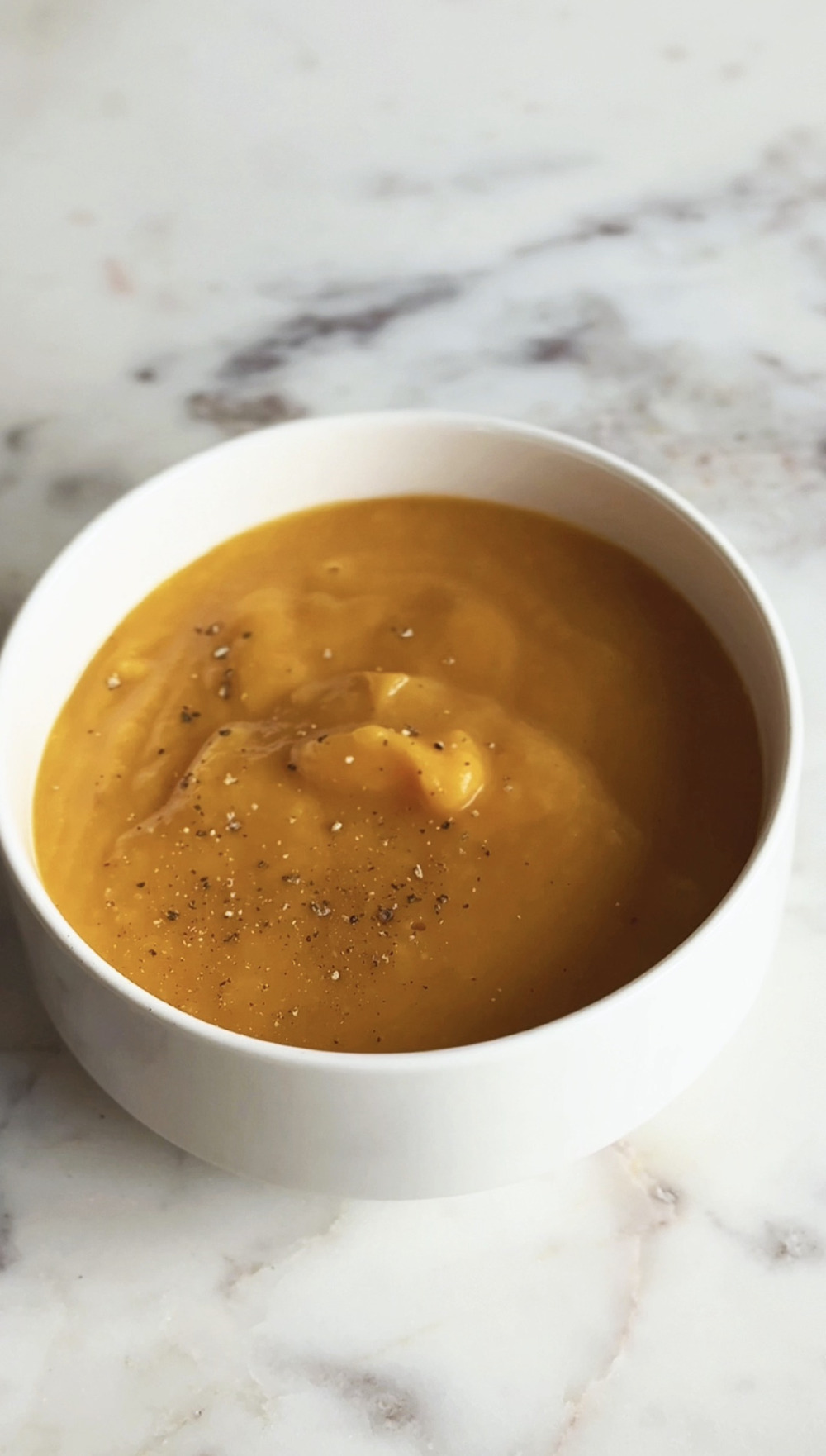 Finished butternut squash soup in a white bowl on marble with cracked black pepper