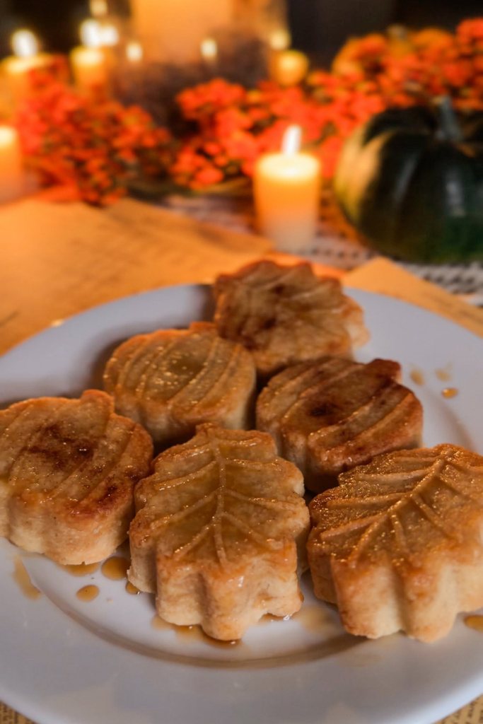 Six maple glazed shortbread leaves and pumpkins arranged on a white plate