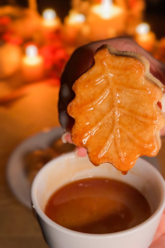 Glossy maple dipped oak leaf shortbread cookie lifted from the cup of syrup