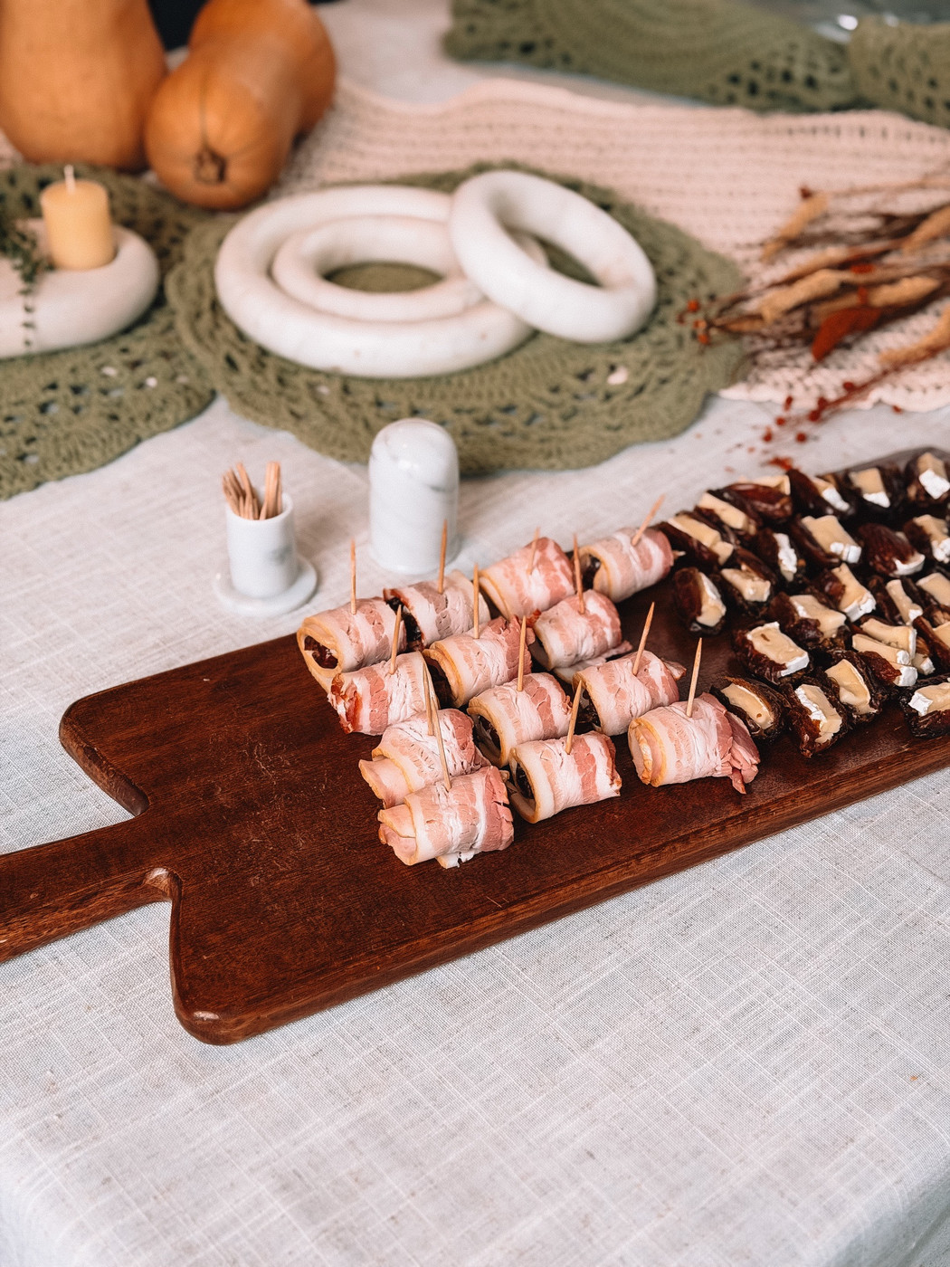Bacon wrapped dates on a wooden board on a fall table with candles and butternut squash