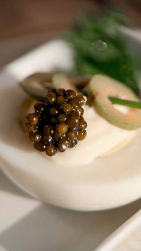 A close up of dark caviar pearls spooned onto cream on a white plate.