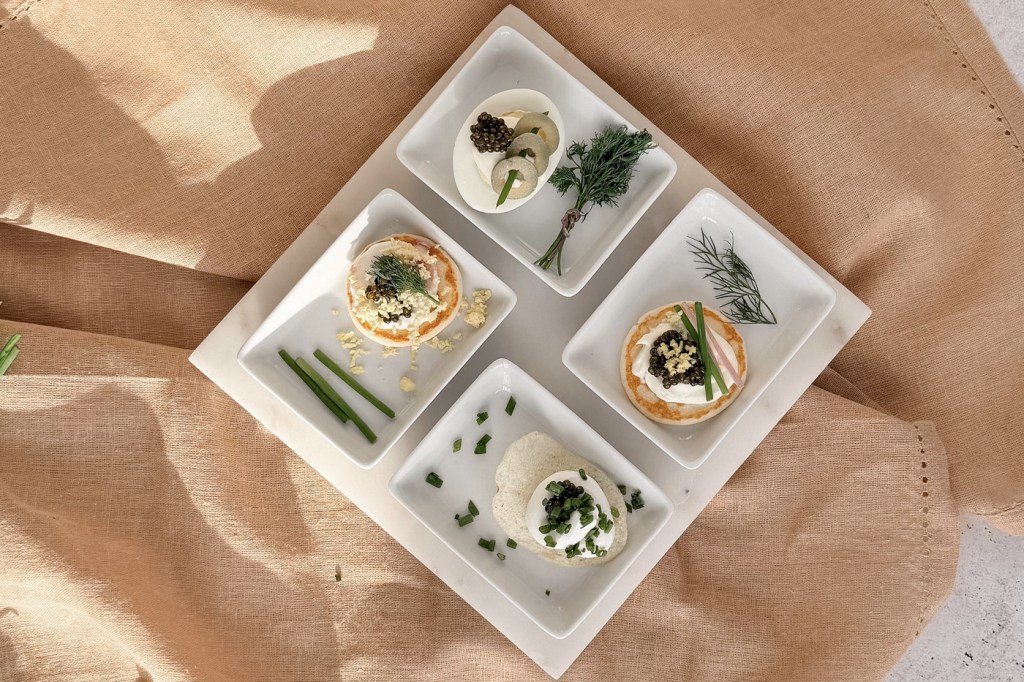 A white four section tray holding four different caviar bites, on tan linen.