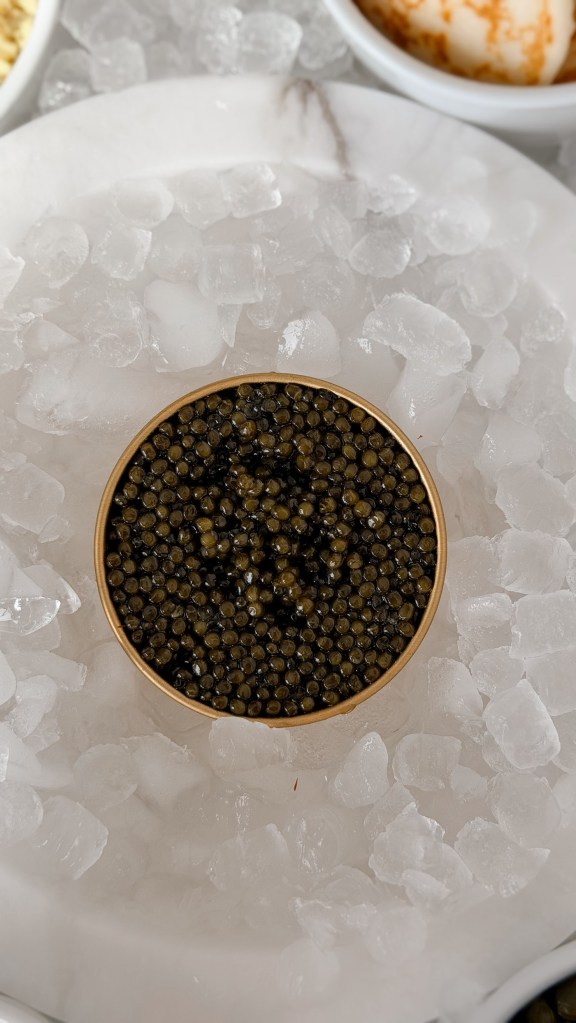 An open gold tin of caviar sitting in a bed of crushed ice, seen from above.