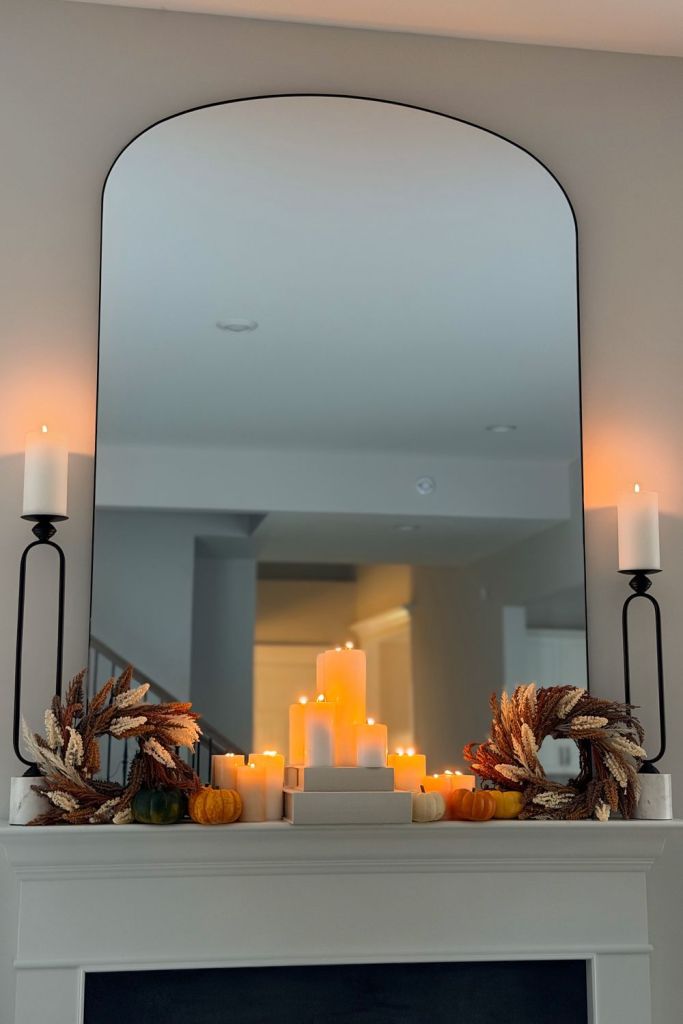 Fall mantel styled with candlesticks, wheat wreaths and mini pumpkins under an arched mirror