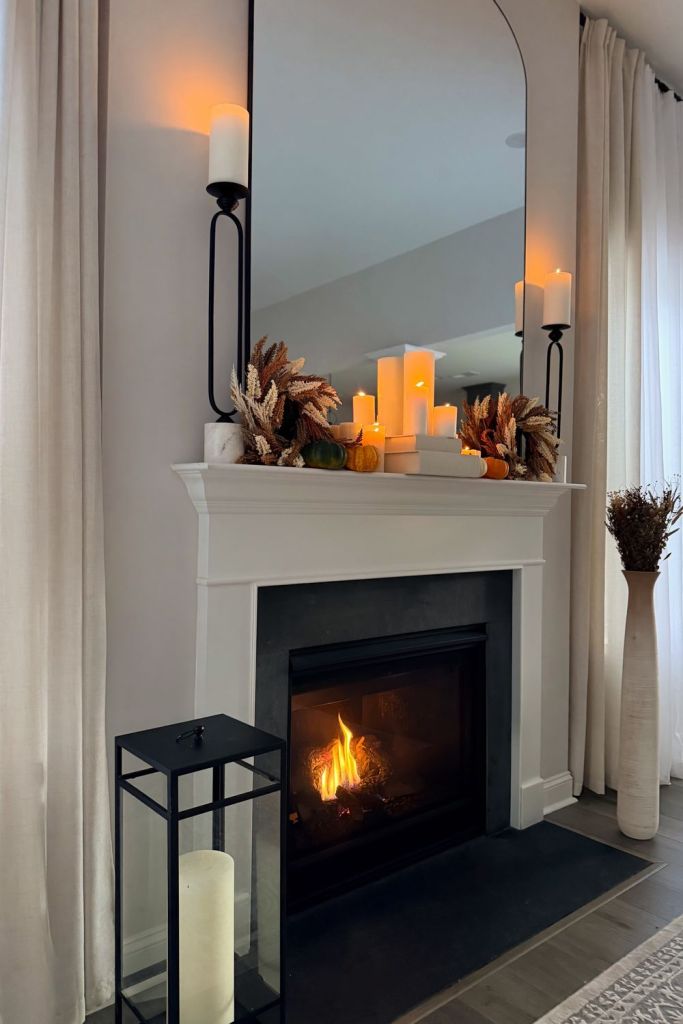 Fireplace with a tall floor lantern on the hearth and dried stems in a vase
