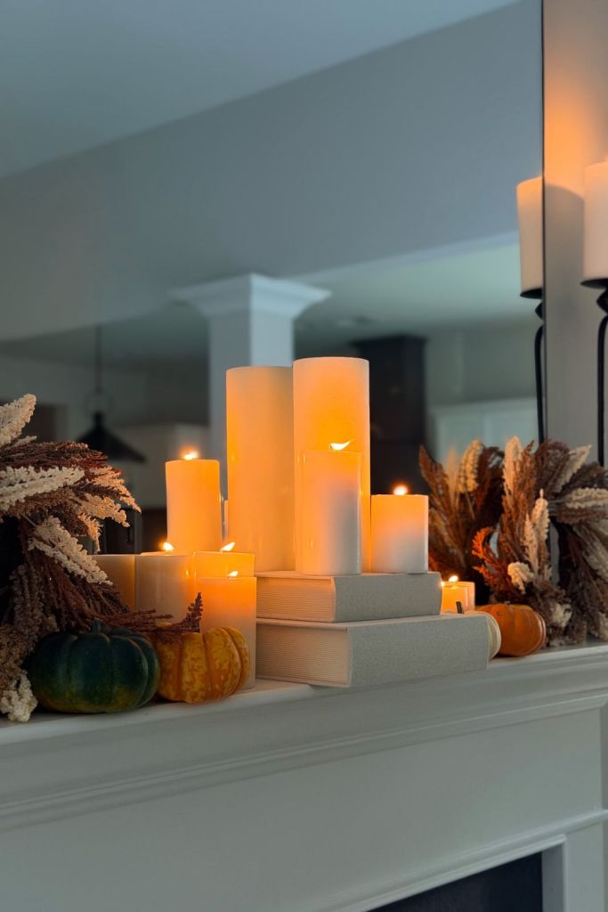 Cluster of pillar candles on stacked books with mini pumpkins on a white mantel