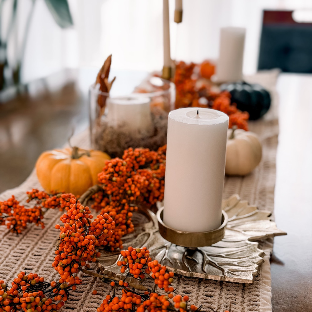 White pillar candle on a brass leaf holder surrounded by berries