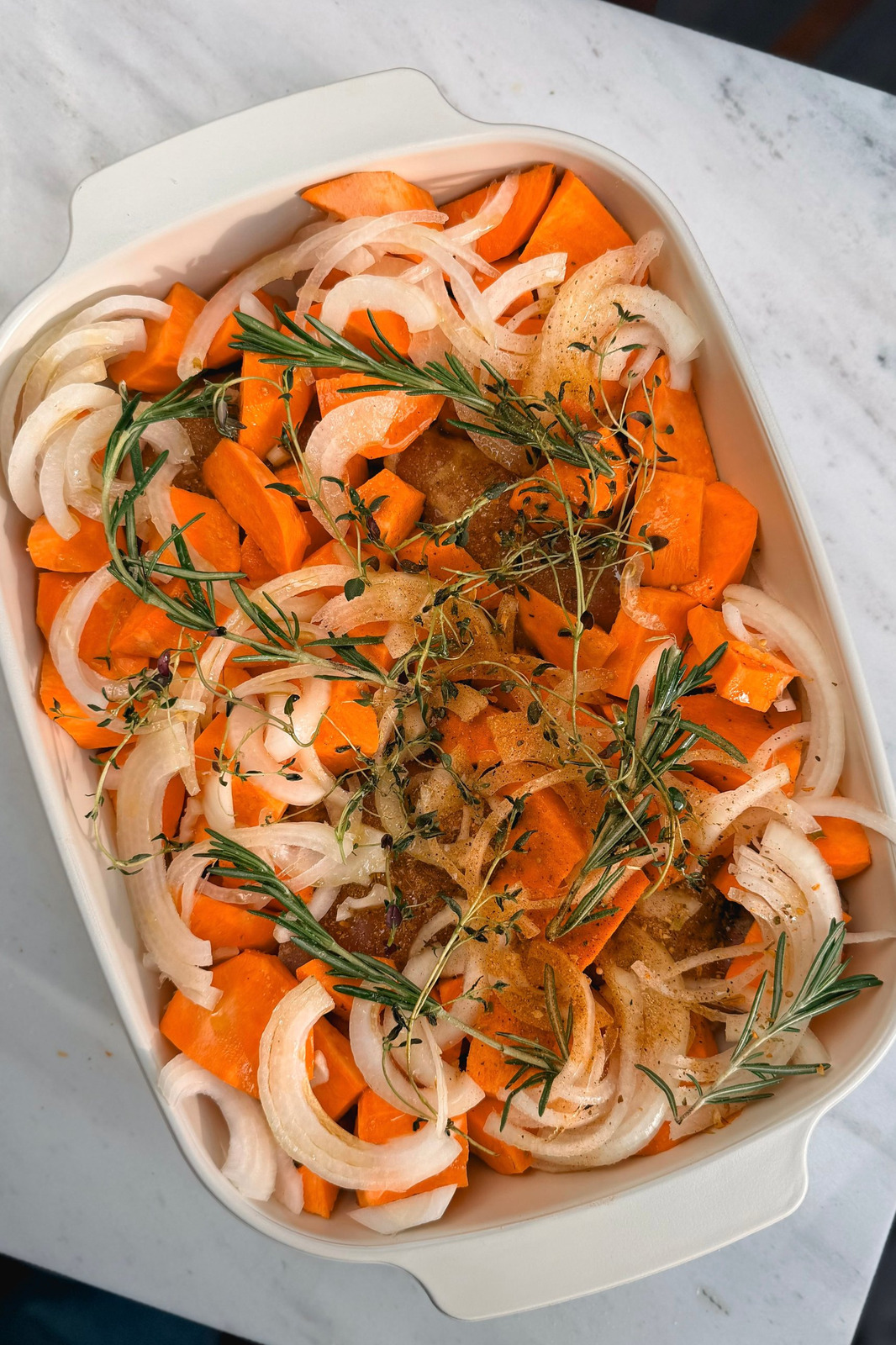 Raw chicken, chopped sweet potatoes, sliced onion, thyme and rosemary in a cream baking dish before going into the oven