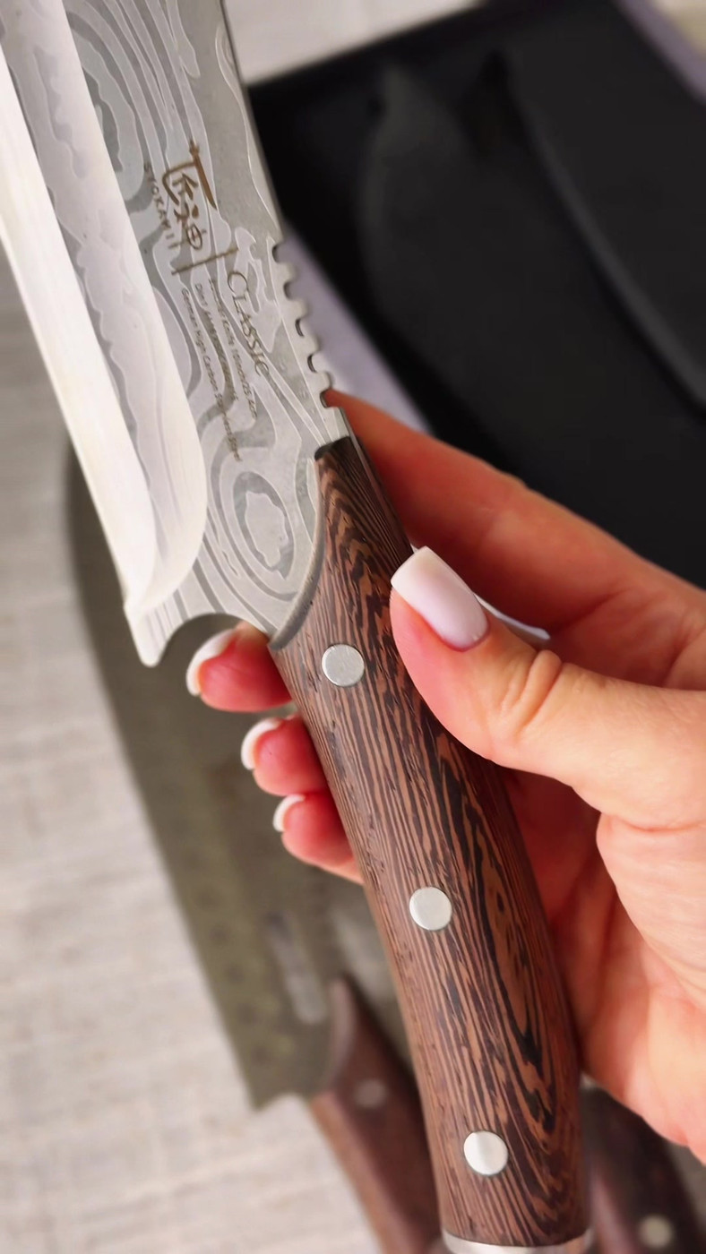 Holding a SYOKAMI knife by its dark wenge wood handle with three rivets, blade pattern visible